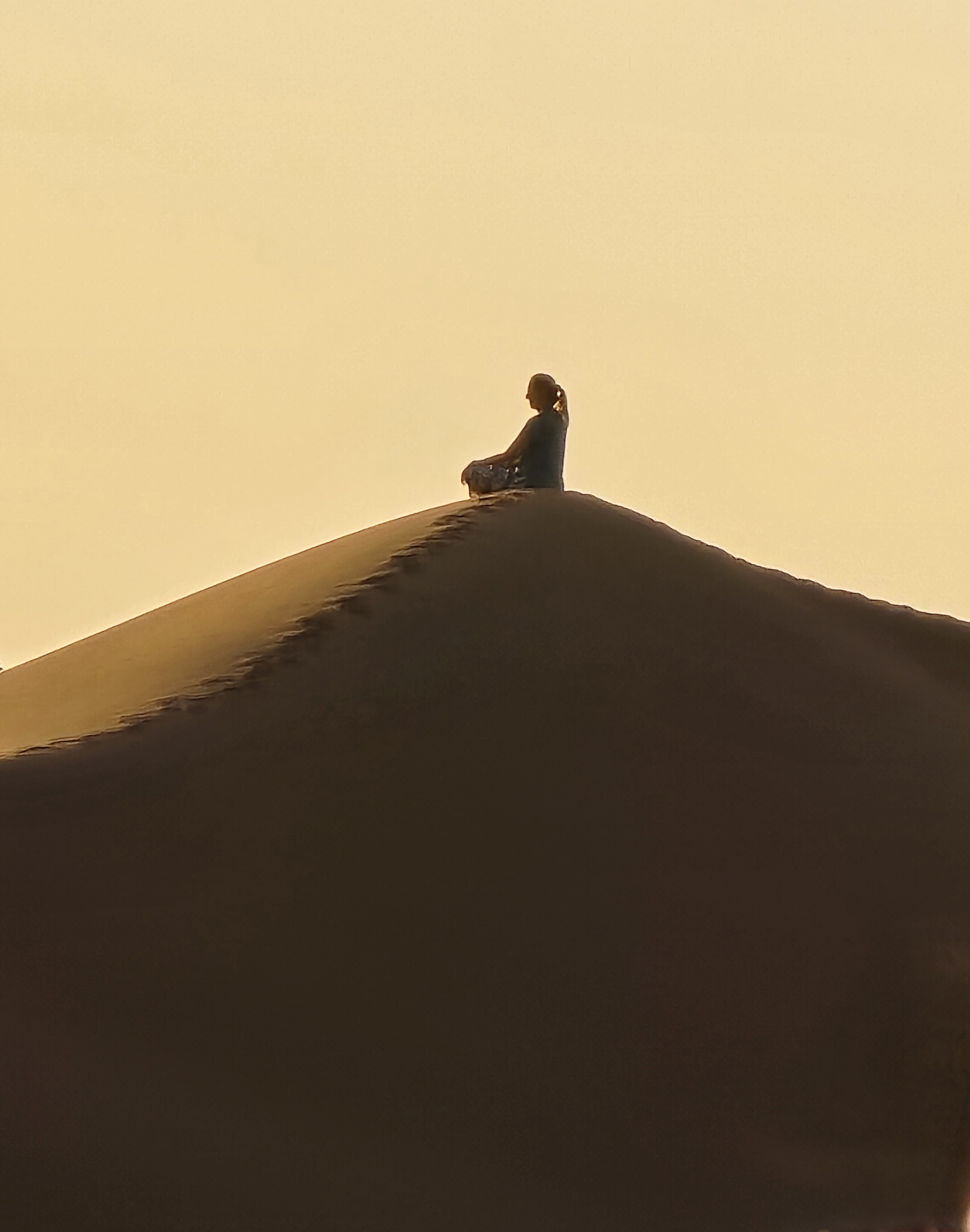 Une silhouette assise sur une dune de sable au coucher du soleil.
